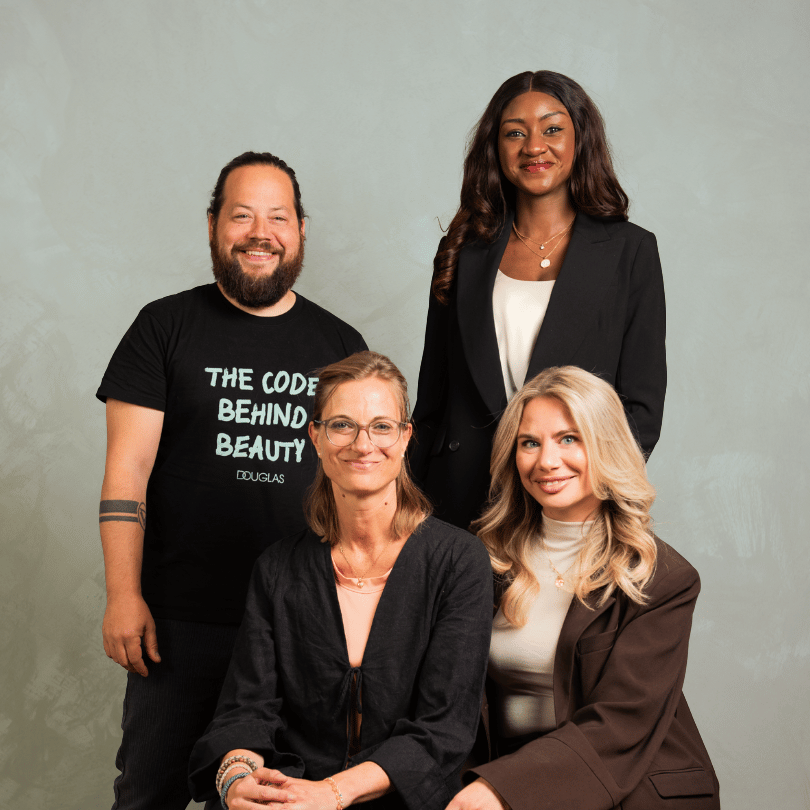 Vier Teammitglieder von DOUGLAS bei einem Gruppenfoto — Tim Joussen und Aiseosa Marcella Cole stehend, Mareike Mende-Ratnam und Anna Maria Tamburrelli sitzend im Vordergrund.